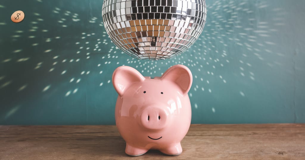 A pink piggy bank sitting on a wooden surface under a sparkling disco ball, casting light reflections on a teal background. Piggy banks are used for stress-free budgeting and disco balls for holiday celebrations