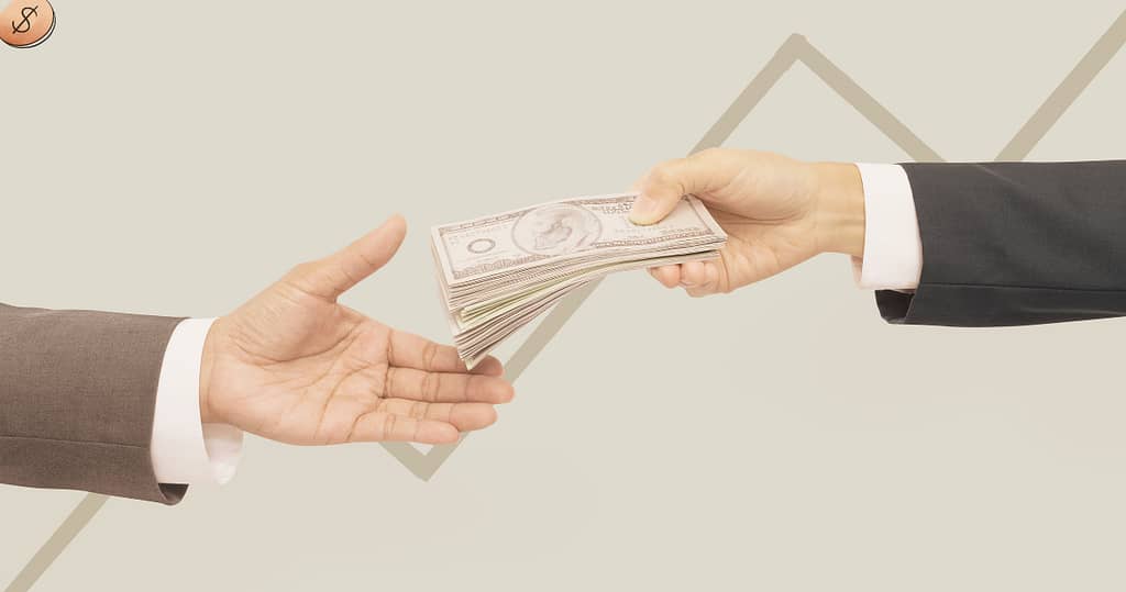 two hands passing a pile of cash to each other on payday to resemble payroll linked payments