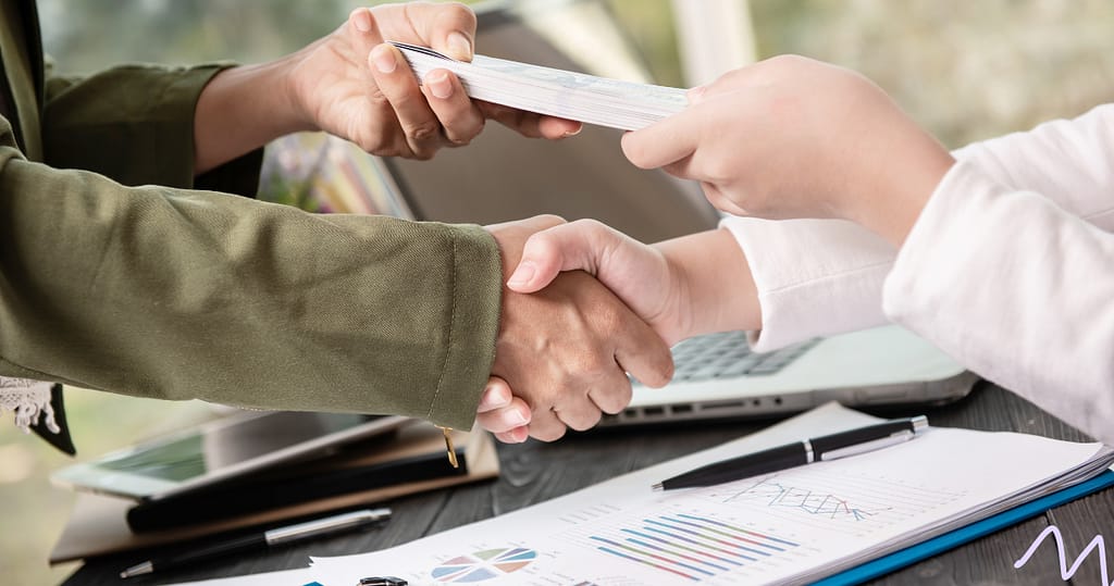 A close-up of two people shaking hands as one hands over a stack of cash, symbolizing transparency and trust in lending, representing what makes a loan "fair"
