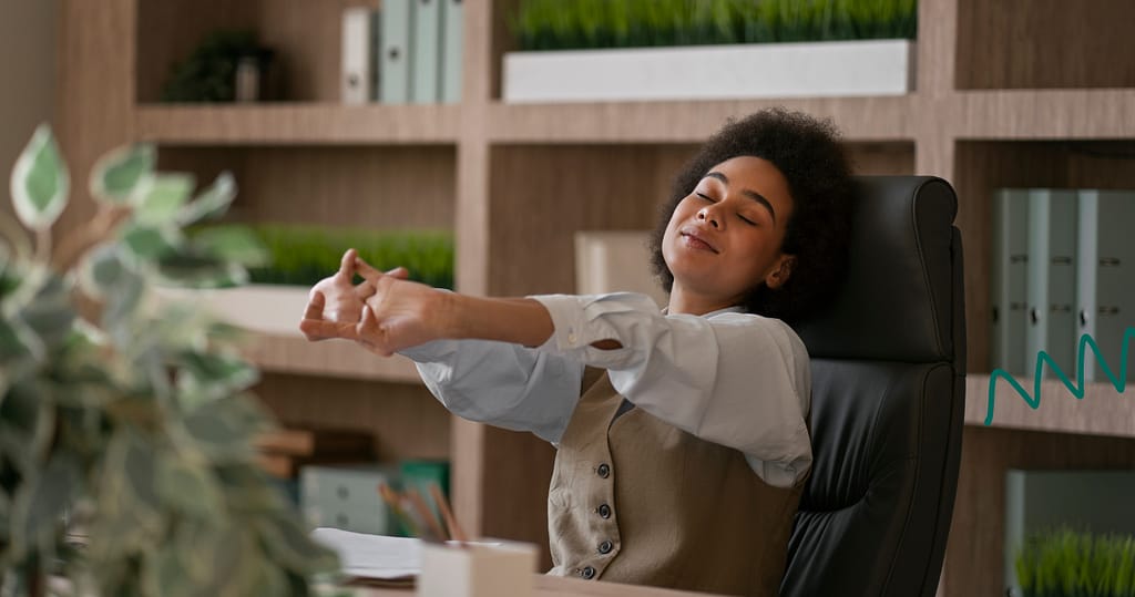 Woman stretching at her desk in office showing relief and reduced workplace stress.