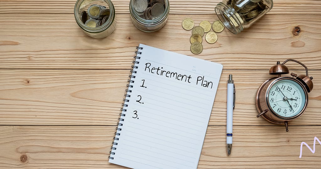 A Retirement Planning Notebook opened on a wooden desk, next to a clock with a numbered list written on it