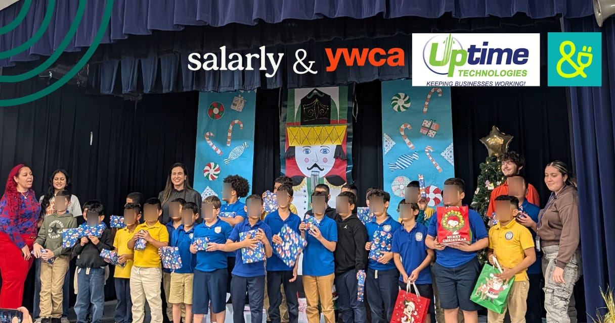 A group of elementary school children standing on a stage holding wrapped holiday gifts during a school holiday celebration
