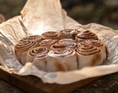A tray of warm, freshly baked cinnamon rolls dusted with sugar, resting on parchment paper. The rolls are golden brown and spiral perfectly, creating an inviting scene.
